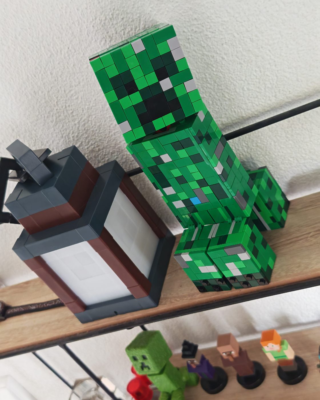 Zelfgebouwde LEGO Minecraft Creeper set 21276 op een wandplank, met Minecraft-figuurtjes op de plank eronder