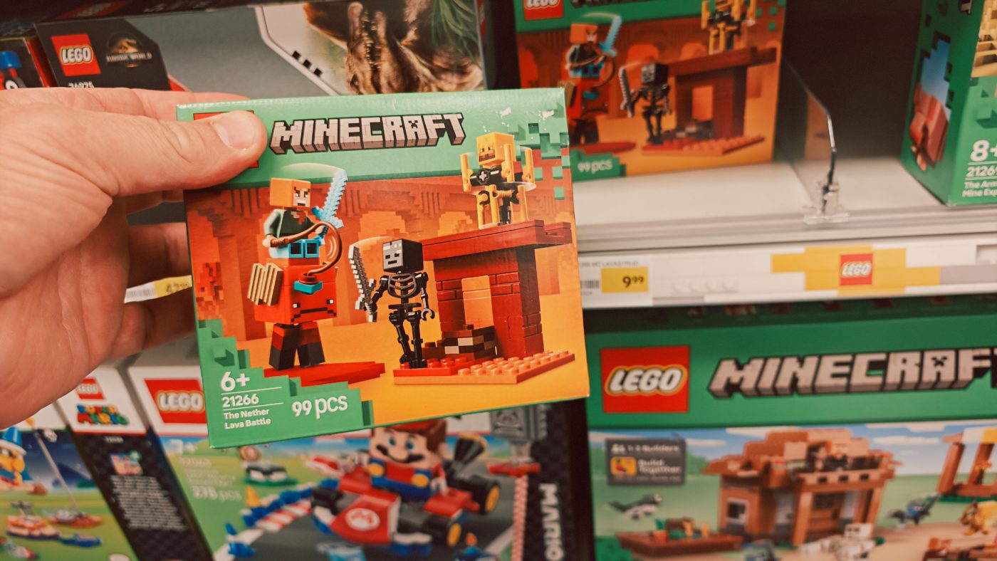 LEGO Minecraft doos 21266 The Nether Lava Battle in de hand, met 6+ en 99 onderdelen zichtbaar op de voorkant
