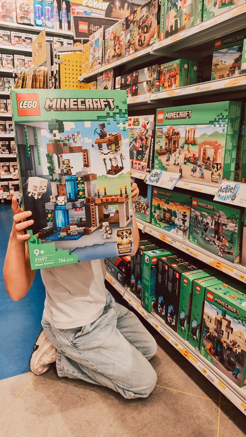 Kind houdt in de winkel een doos van LEGO Minecraft Ghast Station 21597 vast voor het LEGO-schap